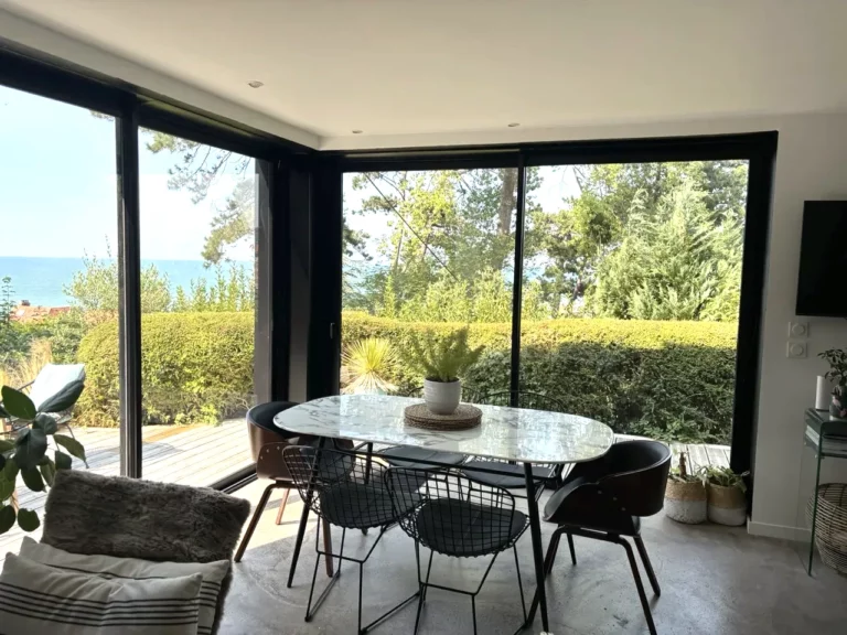 Coin repas devant les baies vitrées ouvertes sur le jardin et la mer, villa Le Carré Vue Mer